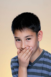 Portrait of laughing boy covering mouth with hand. Photo : Rob Lewine