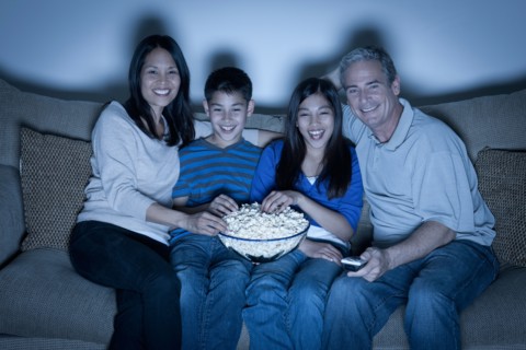 Family sitting on sofa and watching television. Photo : Rob Lewine