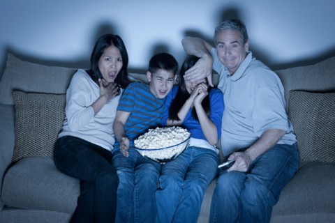 Family sitting on sofa and watching television. Photo : Rob Lewine