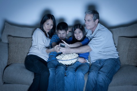 Family sitting on sofa and watching television. Photo : Rob Lewine