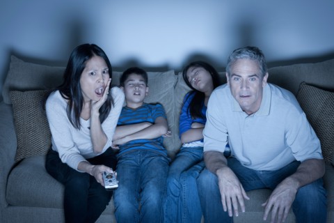 Family sitting on sofa and watching television. Photo : Rob Lewine