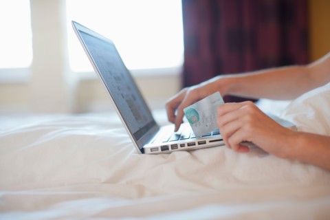 Young woman online shopping while in bed. Photo : Mark de Leeuw