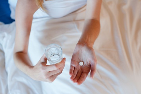 Young woman taking medicine while lying in bed . Photo : Mark de Leeuw