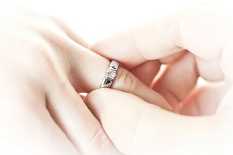 Close-up studio shot of man's hand putting engagement ring on female hand . Photo : Elena Elisseeva