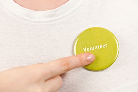 Close-up studio shot female hand pointing at yellow volunteer badge. Photo : Elena Elisseeva