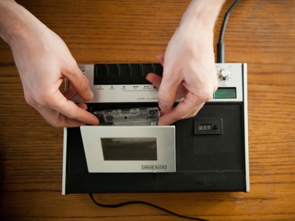 Close-up view of human hands putting tape into old-fashioned tape recorder. Photo : Jessica