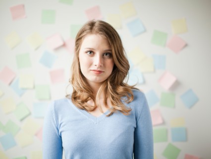 Indoor portrait of young attractive woman standing in f front of wall covered in adhesive notes.