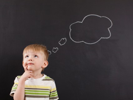 Cute toddler boy (2-3) standing against blackboard with thought bubble written in chalk. Photo :