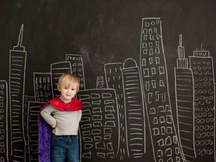 Cute toddler boy (2-3) standing against blackboard with city skyline drawn on it. Photo : Jessica