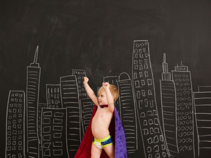 Cute toddler boy (2-3) standing against blackboard with city skyline drawn on it. Photo : Jessica