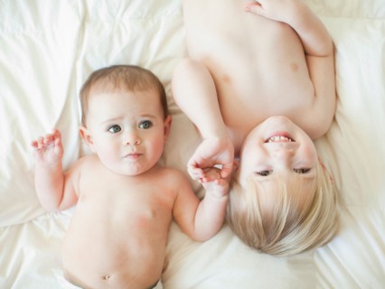 Toddler boy (2-3) lying in bed with baby sister (6-11 months). Photo : Jessica Peterson