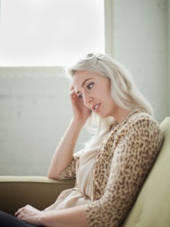 Thoughtful young woman sitting on sofa. Photo : Jessica Peterson