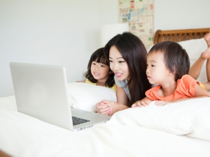 Mother with daughters (2-3, 4-5) lying down in bed, using laptop. Photo : Jessica Peterson