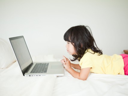 Girl lying down in bed, using laptop (4-5). Photo : Jessica Peterson