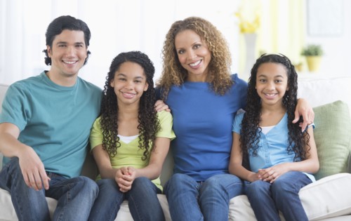 Portrait of parents with daughters (10-13) sitting on sofa.