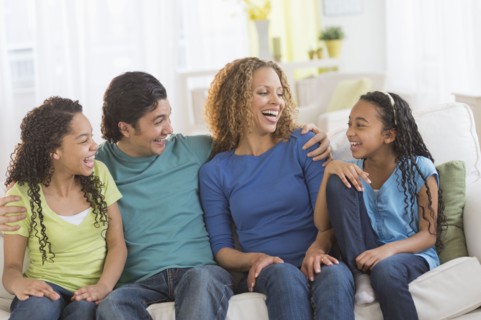 Portrait of parents with daughters (10-13) sitting on sofa.