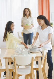 Mother with daughters (10-13) setting table.