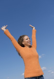 Mature woman with arms raised towards blue sky.