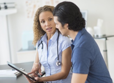 Doctor and patient talking in clinic using tablet pc.