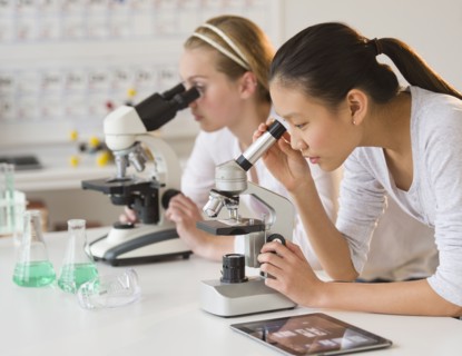 Students (14-17) in chemistry lab using microscope.
