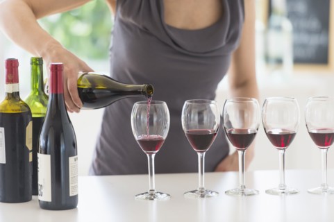 Woman purring red wine into wine glasses.