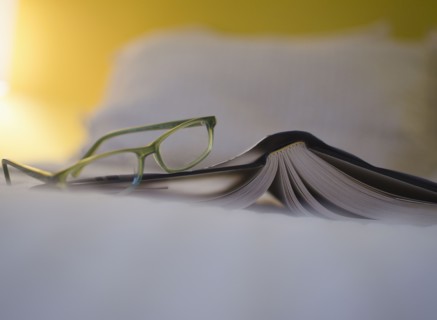 Book and eyeglasses on bed. 
Photo : Jamie Grill