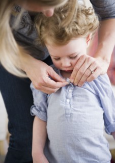 Mother buttoning daughter's (2-3) shirt. 
Photo : Jamie Grill