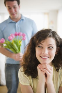 Woman smiling, man with flowers in background. 
Photo : Jamie Grill