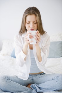 Woman sitting on bed drinking coffee. 
Photo : Jamie Grill