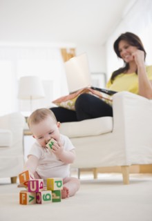 Baby girl (6-11 months) playing with blocks, mother using laptop at home. 
Photo : Jamie Grill