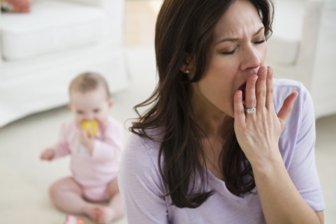 Tired woman yawning, baby daughter (6-11 months) in background. 
Photo : Jamie Grill