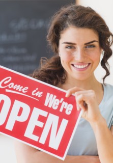 Portrait of smiling waitress showing open sign. 
Photo: Daniel Grill