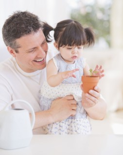 Baby girl (12-17 months) with father watching seedling in pot. 
Photo : Daniel Grill