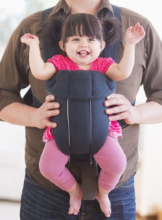 Baby girl (12-17 months) in baby carrier held by her father. 
Photo : Daniel Grill