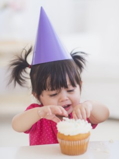 Portrait of baby girl (12-17 months) in party hat eating cupcake. 
Photo : Daniel Grill