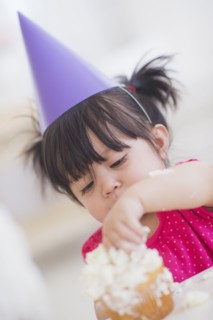 Portrait of baby girl (12-17 months) in party hat eating cupcake. 
Photo : Daniel Grill