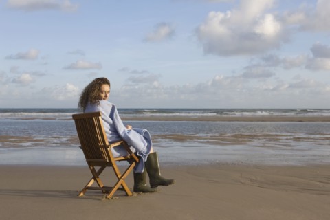 France, Pas-de-Calais, Escalles, Young woman sitting on chair on empty beach. 
Photo : Jan