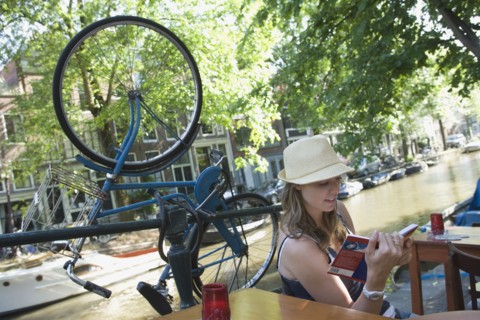 Holland, Amsterdam, Woman with guidebook sitting by canalside. 
Photo : Jan Scherders