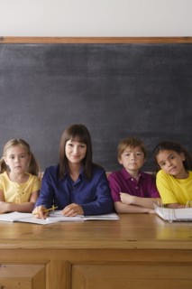 Teacher sitting by desk with group of pupils. 
Photo : Rob Lewine
