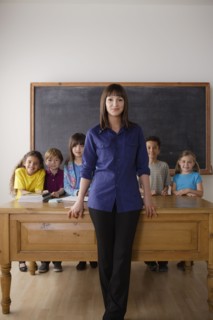 Teacher standing by desk with group of pupils. 
Photo : Rob Lewine