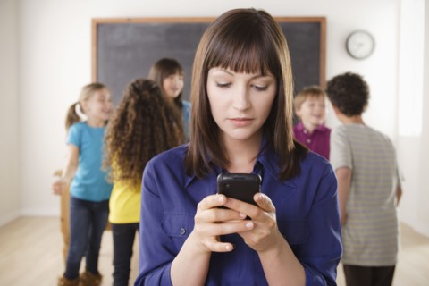 Teacher using mobile phone with group of pupils in background. 
Photo : Rob Lewine