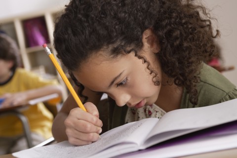 Close-up of writing girl (10-11) with boy (10-11) in background. 
Photo : Rob Lewine