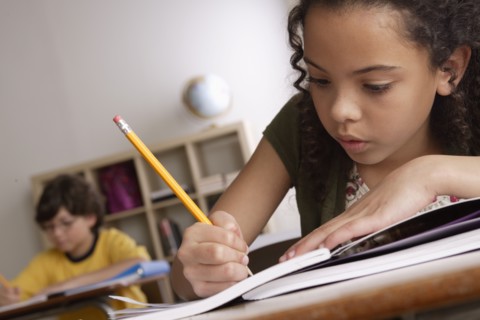 Writing girl (10-11) with boy (10-11) in background. 
Photo : Rob Lewine