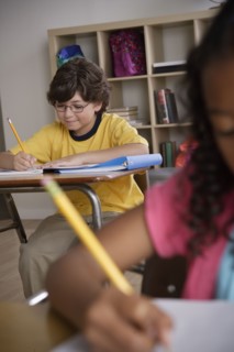 Writing boy (10-11) with girl (10-11) in foreground. 
Photo : Rob Lewine