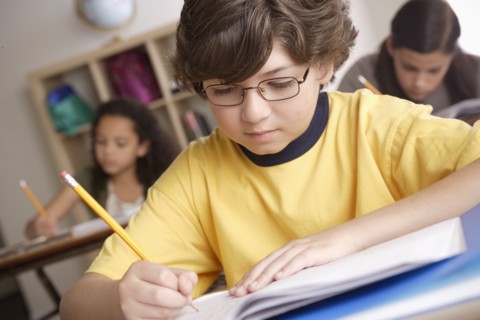 Writing boy (10-11) with girls (10-11, 12-13) in background. 
Photo : Rob Lewine