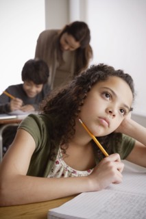 Schoolgirl (10-11) holding pencil with boy (12-13) and teacher in background. 
Photo : Rob Lewine