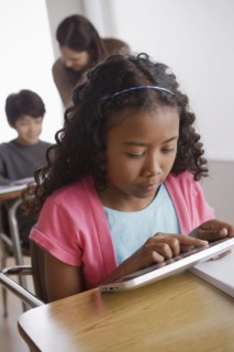 Schoolgirl (10-11) holding digital tablet with boy (12-13) and teacher in background. 
Photo : Rob