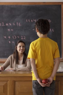 Schoolboy (12-13) holding apple behind back with teacher in background. 
Photo : Rob Lewine