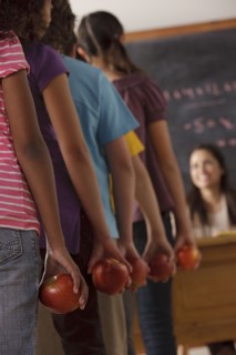 pupils standing in row (10-11, 12-13) holding apple with teacher in background. 
Photo : Rob