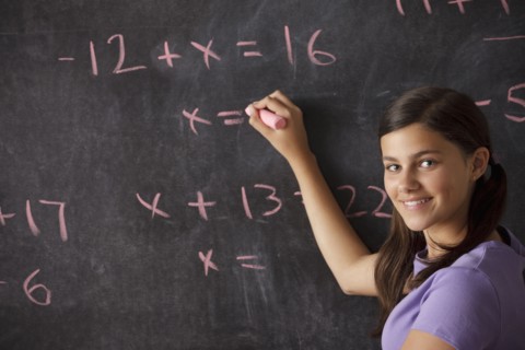 Portrait of schoolgirl (12-13) standing in front of blackboard during math classes. 
Photo : Rob